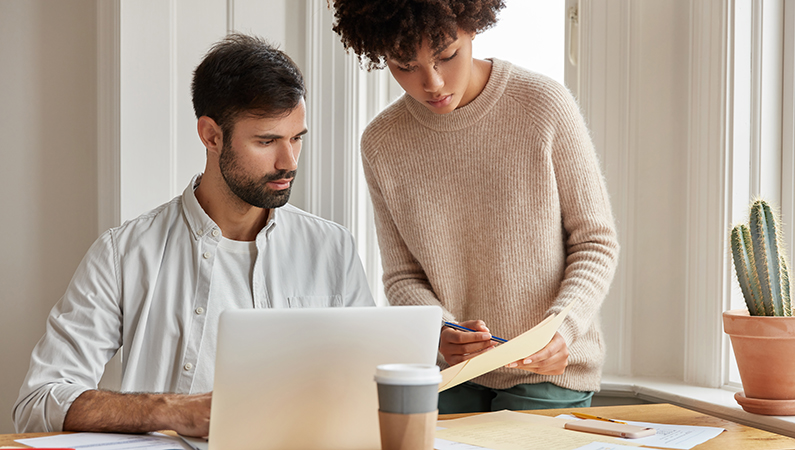 Groupe de personnes en formation professionnelle, écoutant un formateur devant un tableau blanc dans une salle lumineuse.