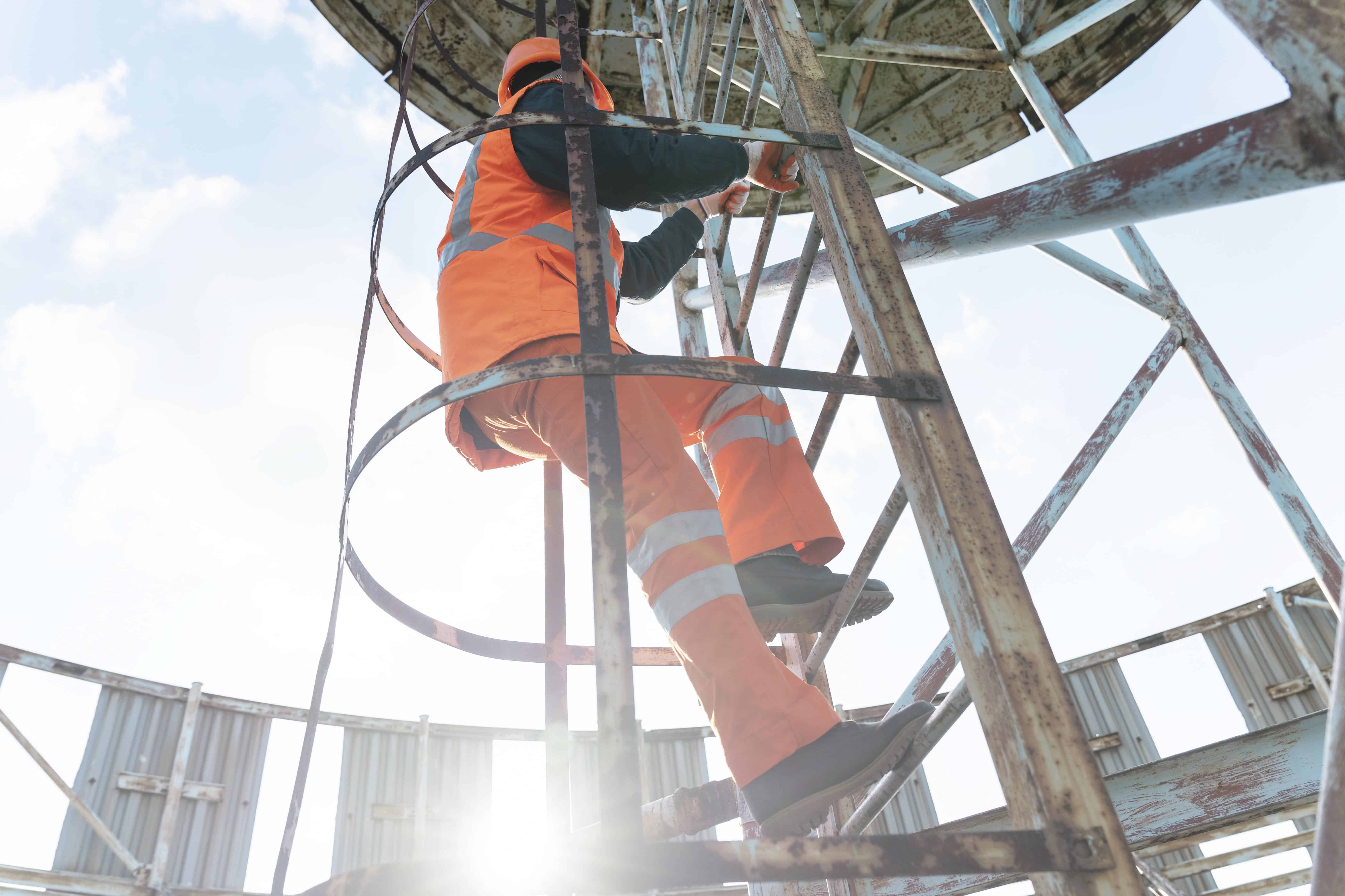 Travailleur en tenue de sécurité grimpant à une échelle sur un site industriel, illustrant la vigilance et la prévention des risques au travail.
